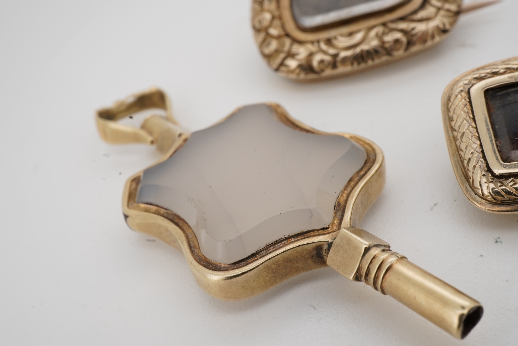 A locket, a watch key and two mourning brooches, the oval locket engraved with foliate details, opening to reveal a glazed panel of hairwork; together with two early 19th century mourning brooches, engraved with flowers